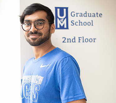 male student standing in front of graduate school sign