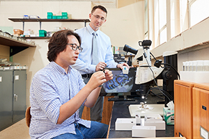 student researcher examines beetle with professor