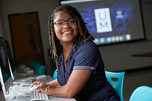 student on computer with UofM logo in background