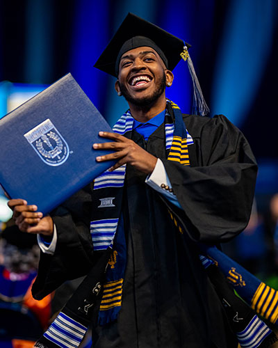 Male student with two stoles laughs after receiving diploma at graduation