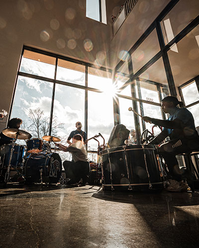 Students rehearse with musical instruments in a sunlit campus building.