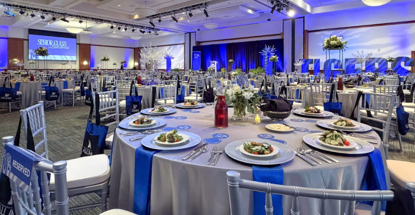 Photo of UC Ballroom decorated for a luncheon with large projection screen and a stage