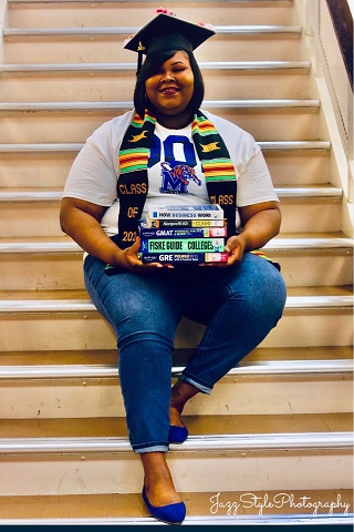 Lakeshia sits with textbooks in her lap and a cap on for graduation pictures