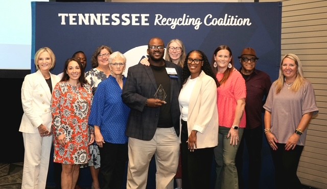 Group photo of Tennessee Delta Alliance team members posing in front of a blue backdrop, all smiling.