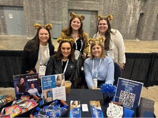 AuD students (standing) and faculty (seated) at the UofM recruitment table at ASHA 2025, Washington DC AuD students (standing) and faculty (seated) at the UofM recruitment table at ASHA 2025, Washington DC