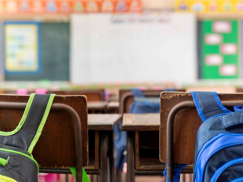 Recommended size: 800 × 600 px Backpacks hang from chairs in an elementary school classroom.