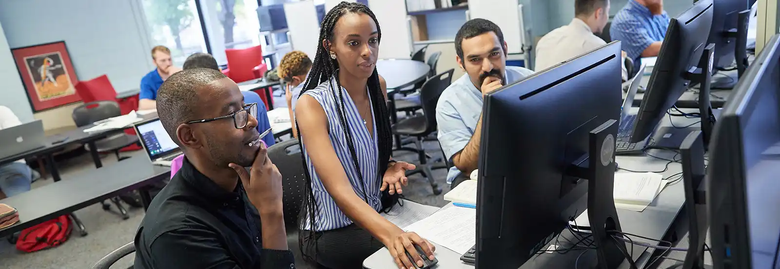 three students in a classroom looking at a computer