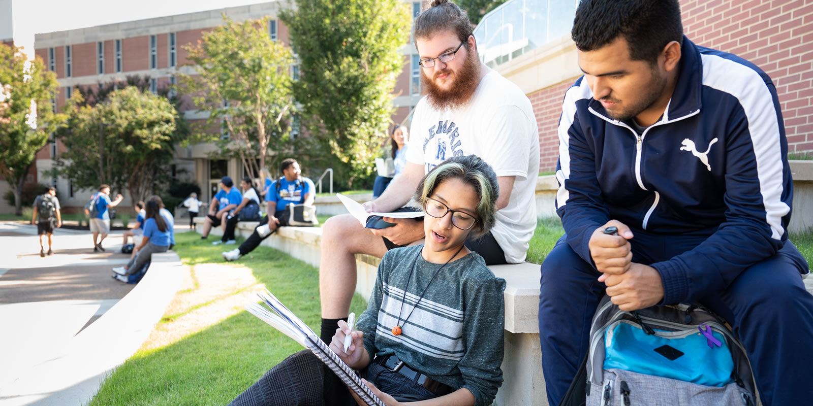 Students seated outdoors looking at a notebook