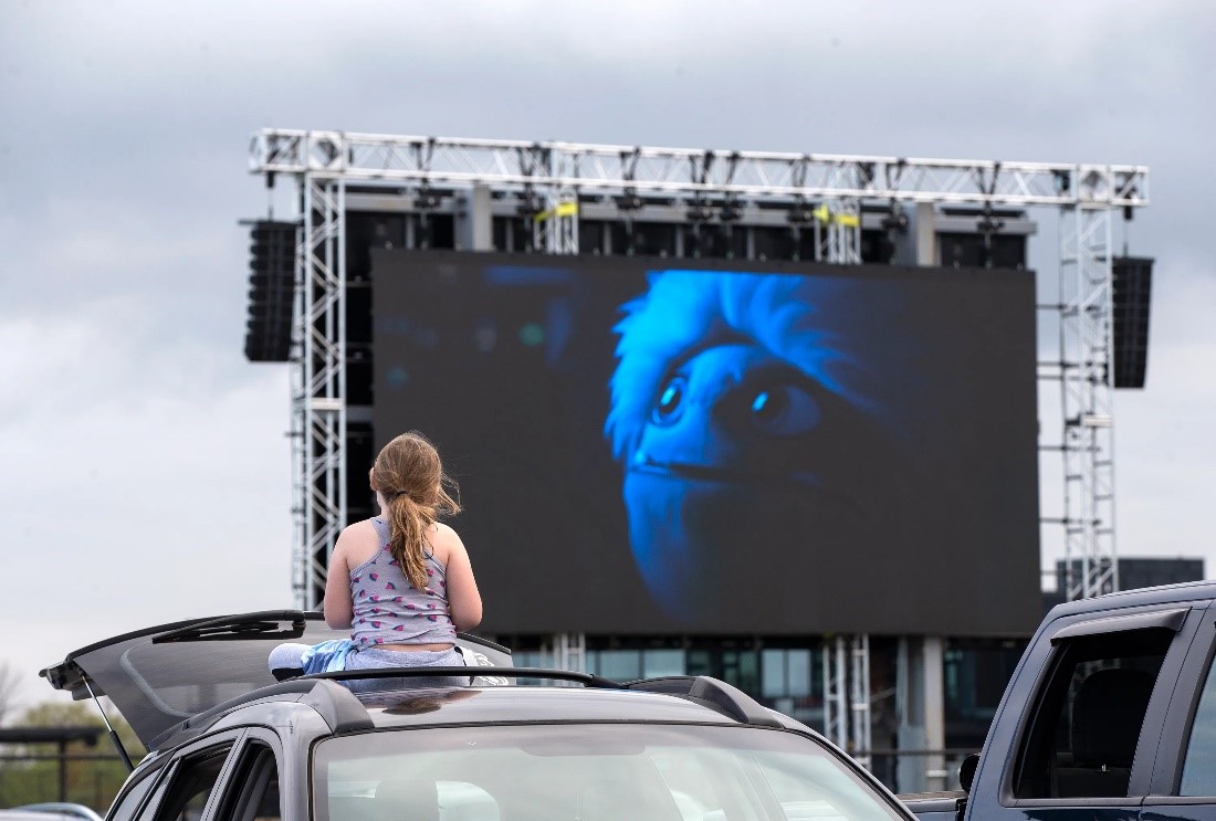 Woman sitting in car watching movie on screen at drive in movie