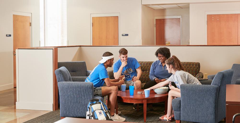 Living Learning Complex (LLC) Lounge Area - four students sitting around coffee table playing challenging competitive games and relaxing.