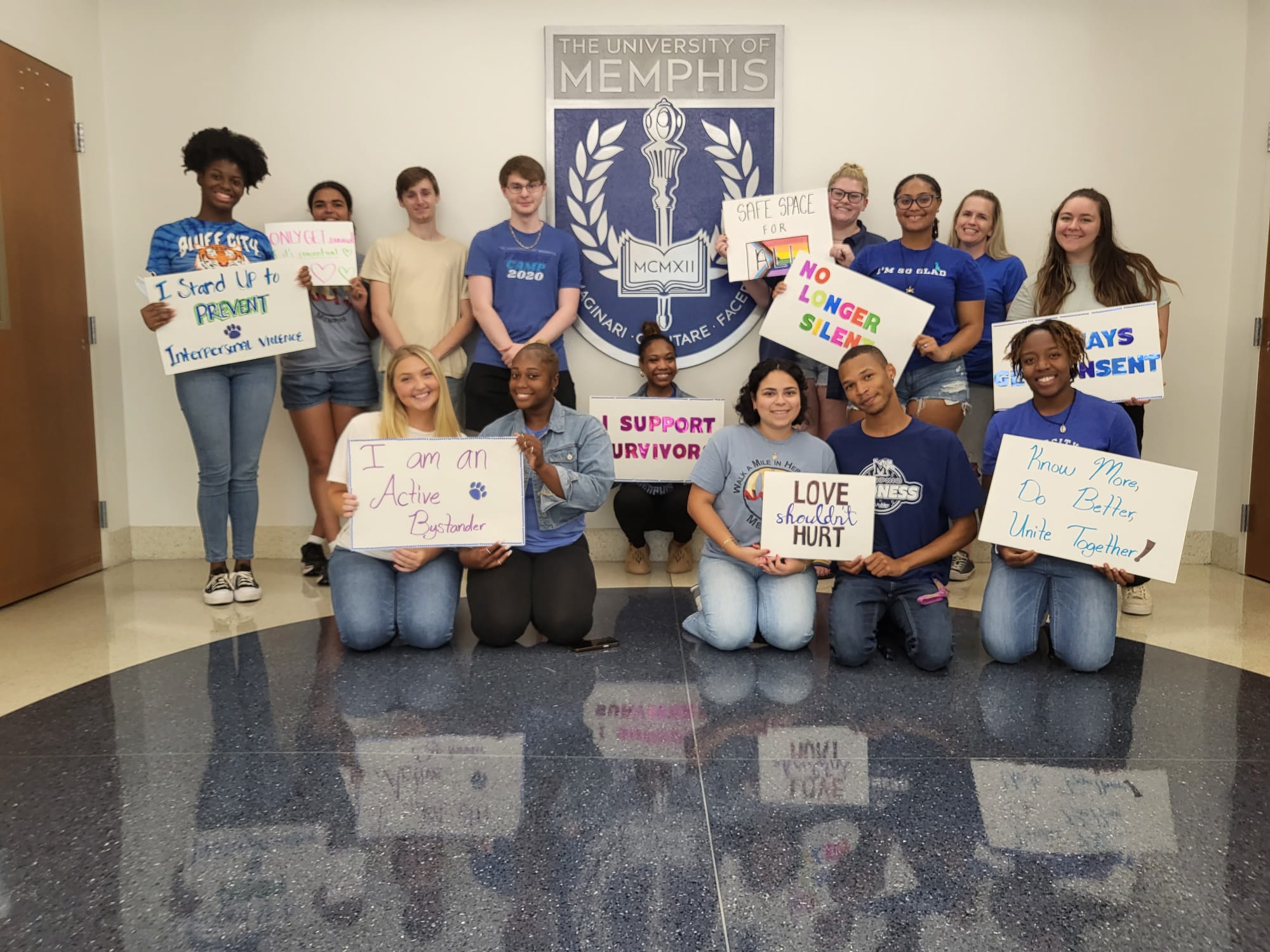 multiple UofM students with a sign saying "Know More, Do Better"