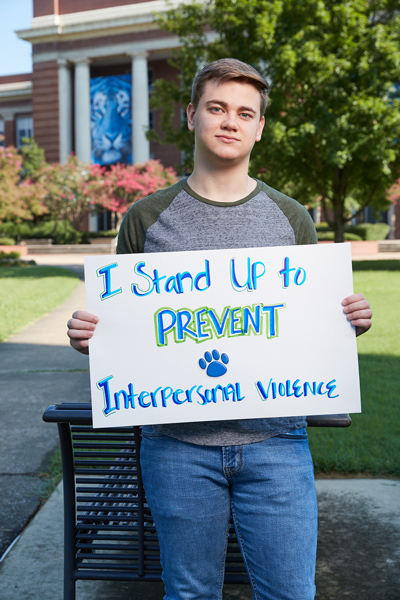 student holding sign that says "I stand up to prevent interpersonal violence"