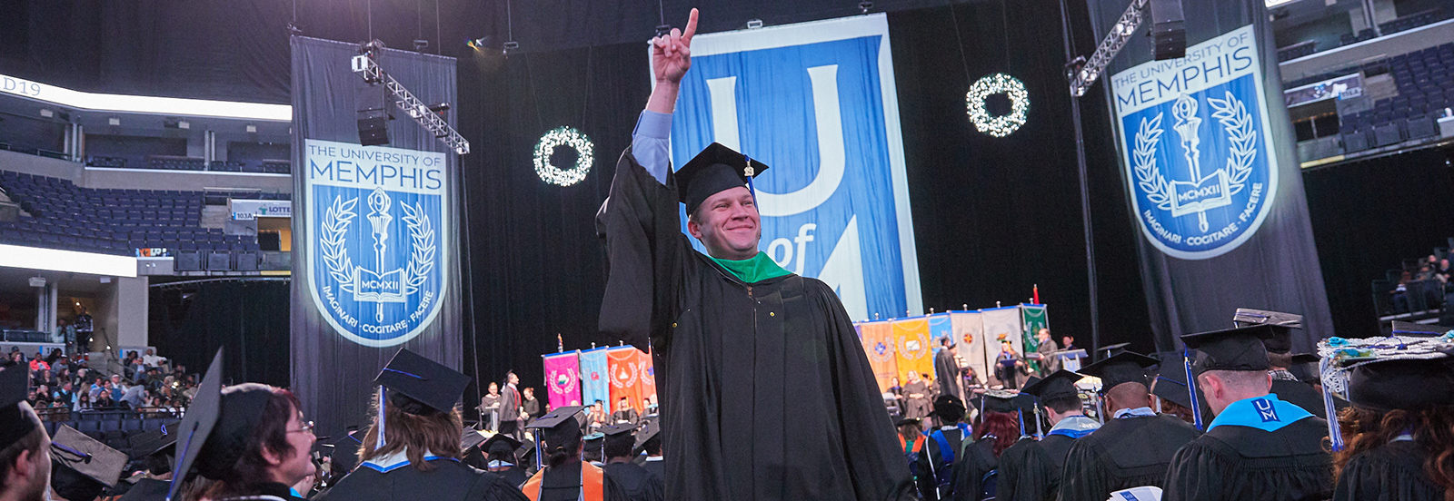 photo of male graduate holding one finger in the air gesturing "number 1" after receiving his diploma at Commencement