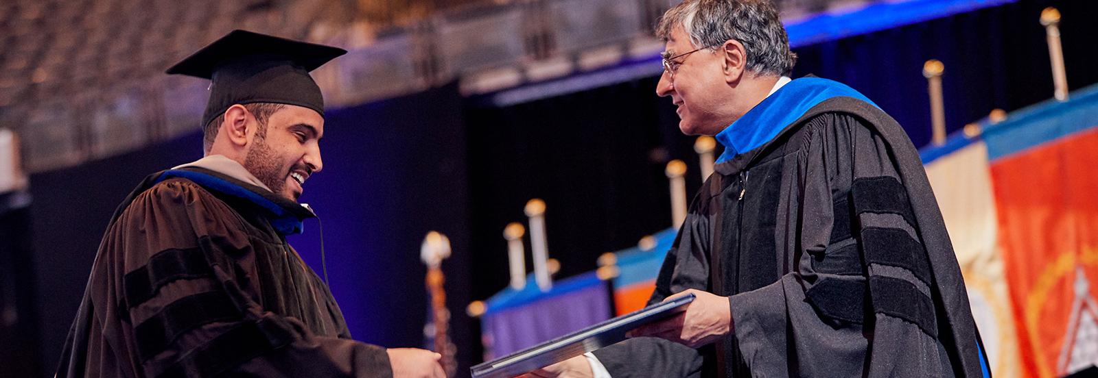 male student shakes hand of dean while receiving diploma at Commencement