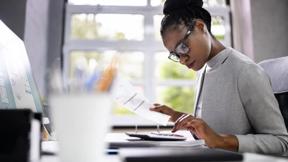 Women with glasses leaning over desk with paperwork and a laptop