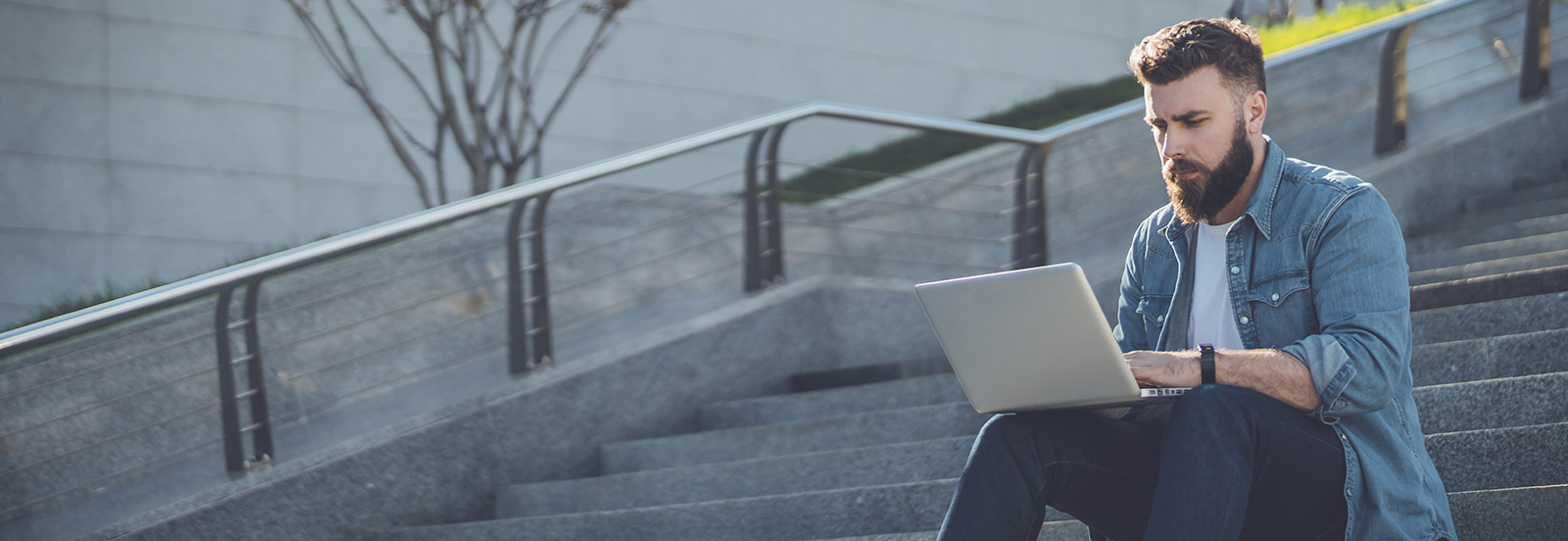 male student sitting on outdoor steps working on laptop