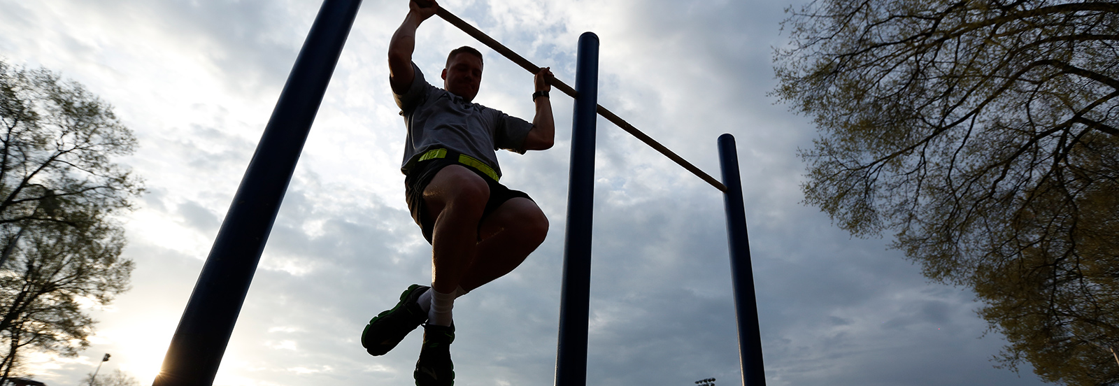 ROTC member working out on pull-up bar; subject is very shadowed due to lighting in the background